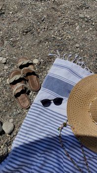Flat lay of sandals, hat, and sunglasses on a striped towel by the beach.