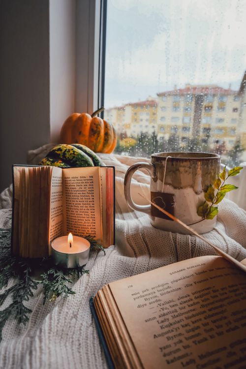 Free A warm and inviting autumn setting featuring books, pumpkins, and a candle by a window. Stock Photo
