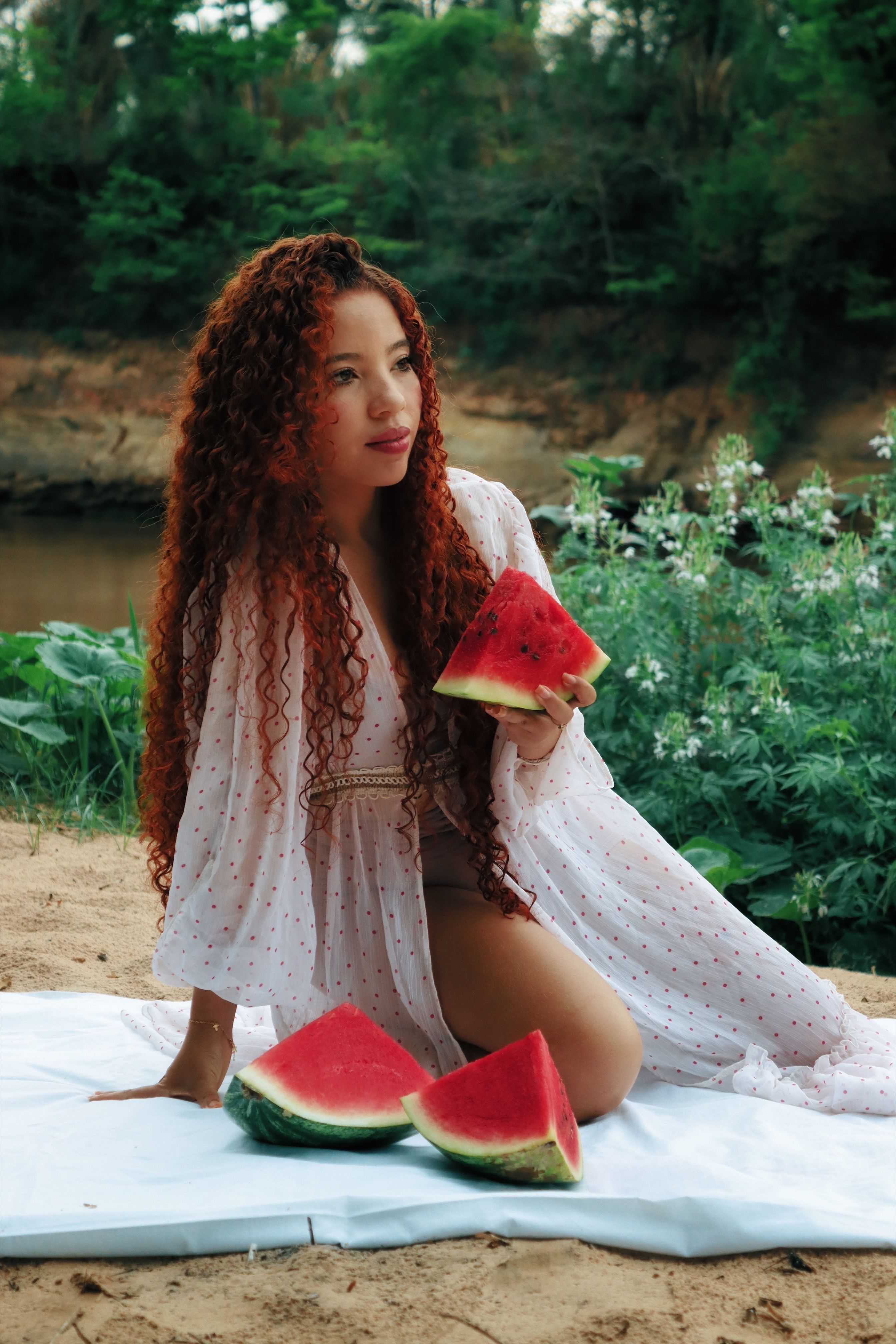 A young woman enjoys watermelon on a summer day by a river.