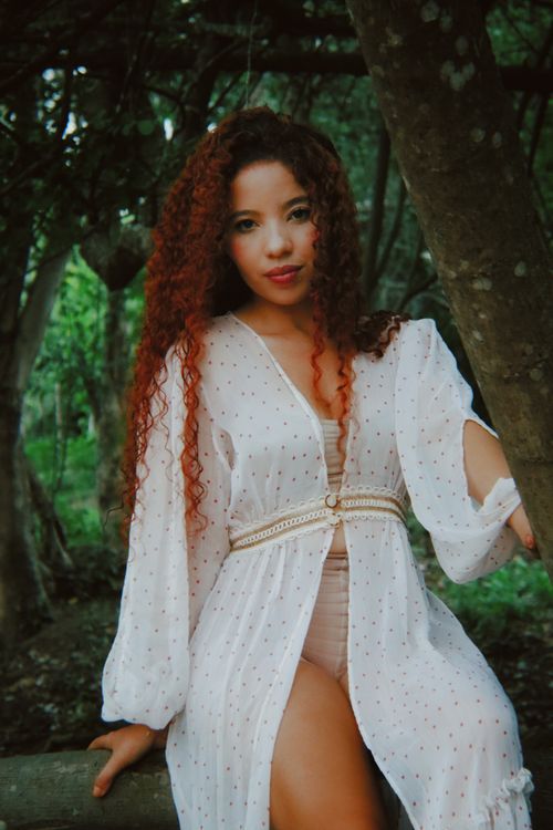 Free Fashionable woman with curly hair in a white dress in a lush green forest. Stock Photo