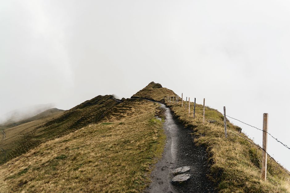 A scenic mountain trail lined with barbed wire fence under misty weather conditions.
