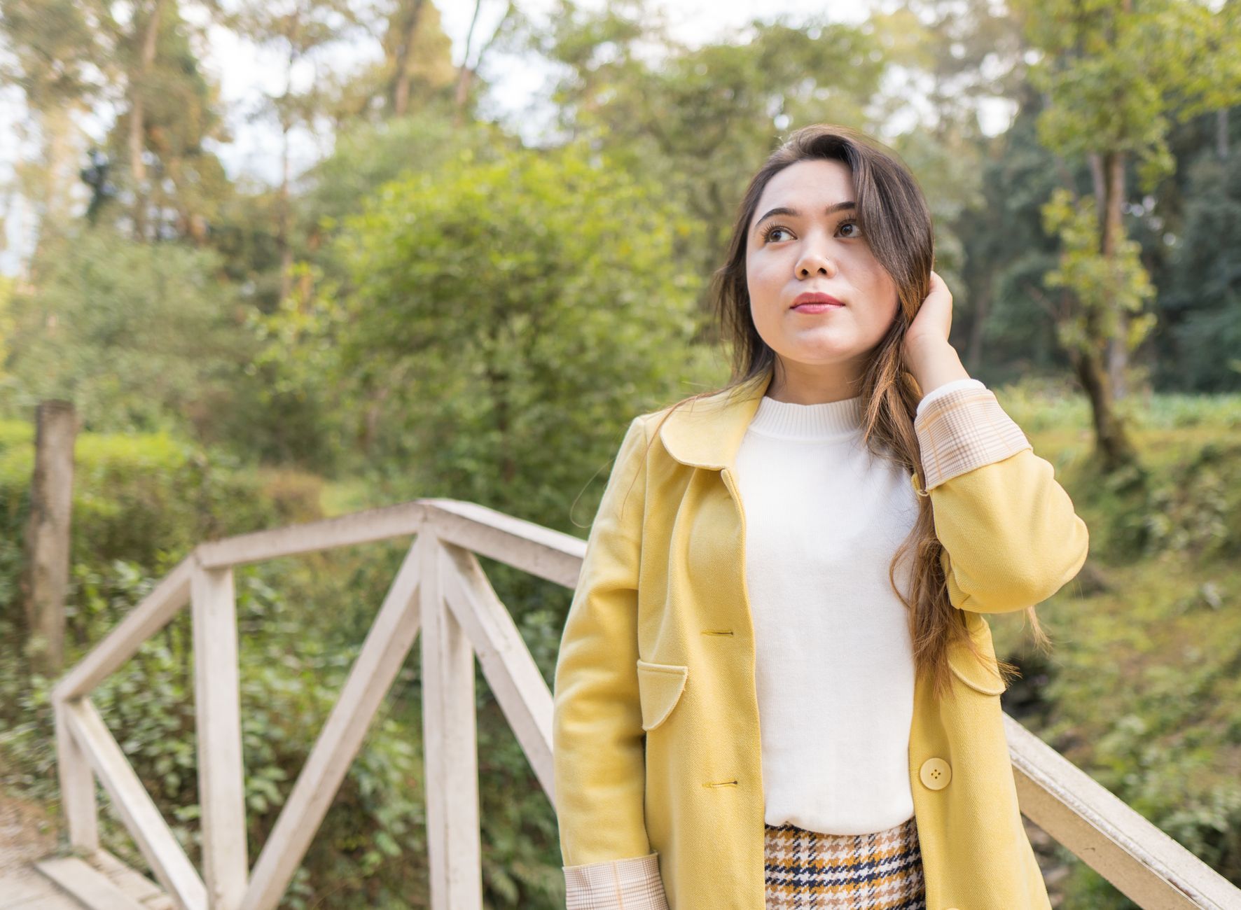 Young woman in a yellow coat stands on a wooden bridge in a lush park in Kathmandu, Nepal.