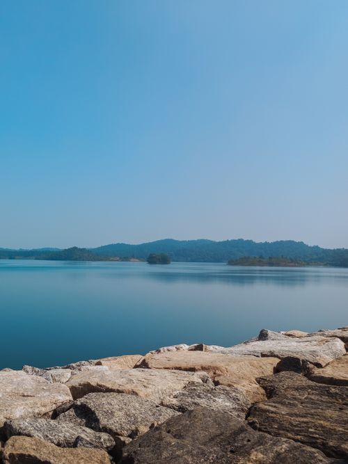Free Tranquil view of Purulia lake with rocky shoreline and distant hills under clear blue sky. Stock Photo
