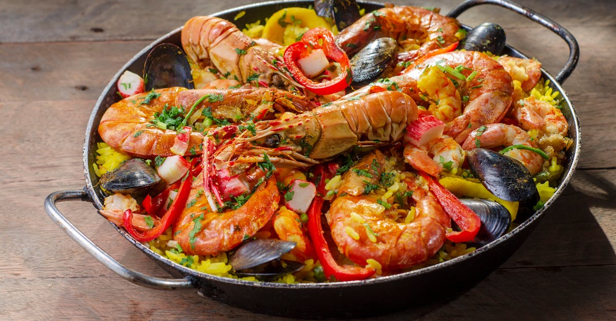 A large, colorful paella pan filled with a rich assortment of seafood including shrimp, mussels, clams, and squid, cooked with saffron-infused rice.