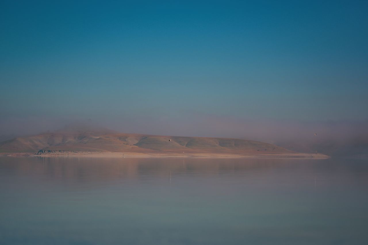 Peaceful misty landscape over calm water reflecting mountains at dawn