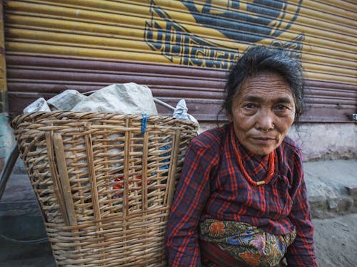 Free An Elderly Woman with Nose Piercing Sitting Beside a Basket while Looking at the Camera Stock Photo