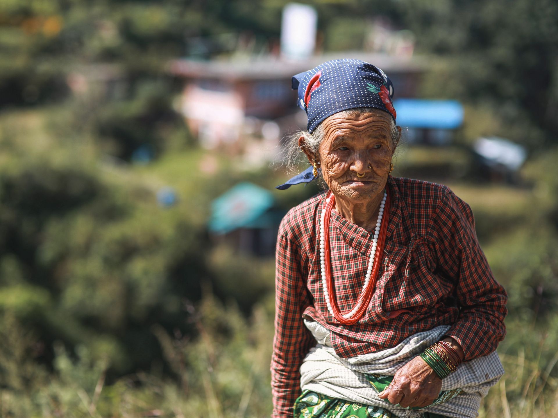 Elderly woman wearing traditional clothes in a rural outdoor setting with a headscarf.