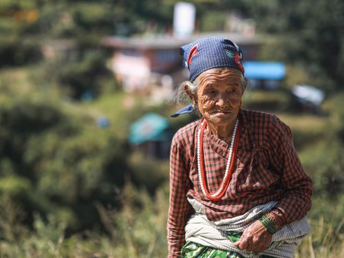 Free Elderly woman wearing traditional clothes in a rural outdoor setting with a headscarf. Stock Photo