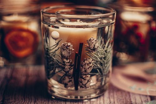 Free Stylish candle in a glass with natural pinecone and cinnamon decorations, ideal for holiday ambiance. Stock Photo
