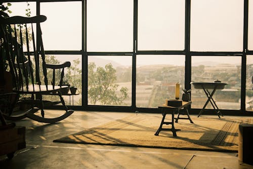 View of a Rocking Chair and Antique Items in a Room with Large Windows 