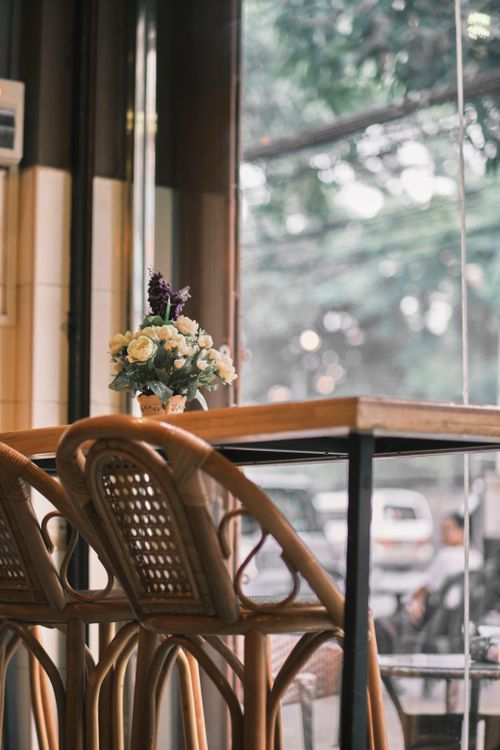 Free Charming cafe interior with wicker chairs and floral decor by a window, creating a serene ambiance. Stock Photo