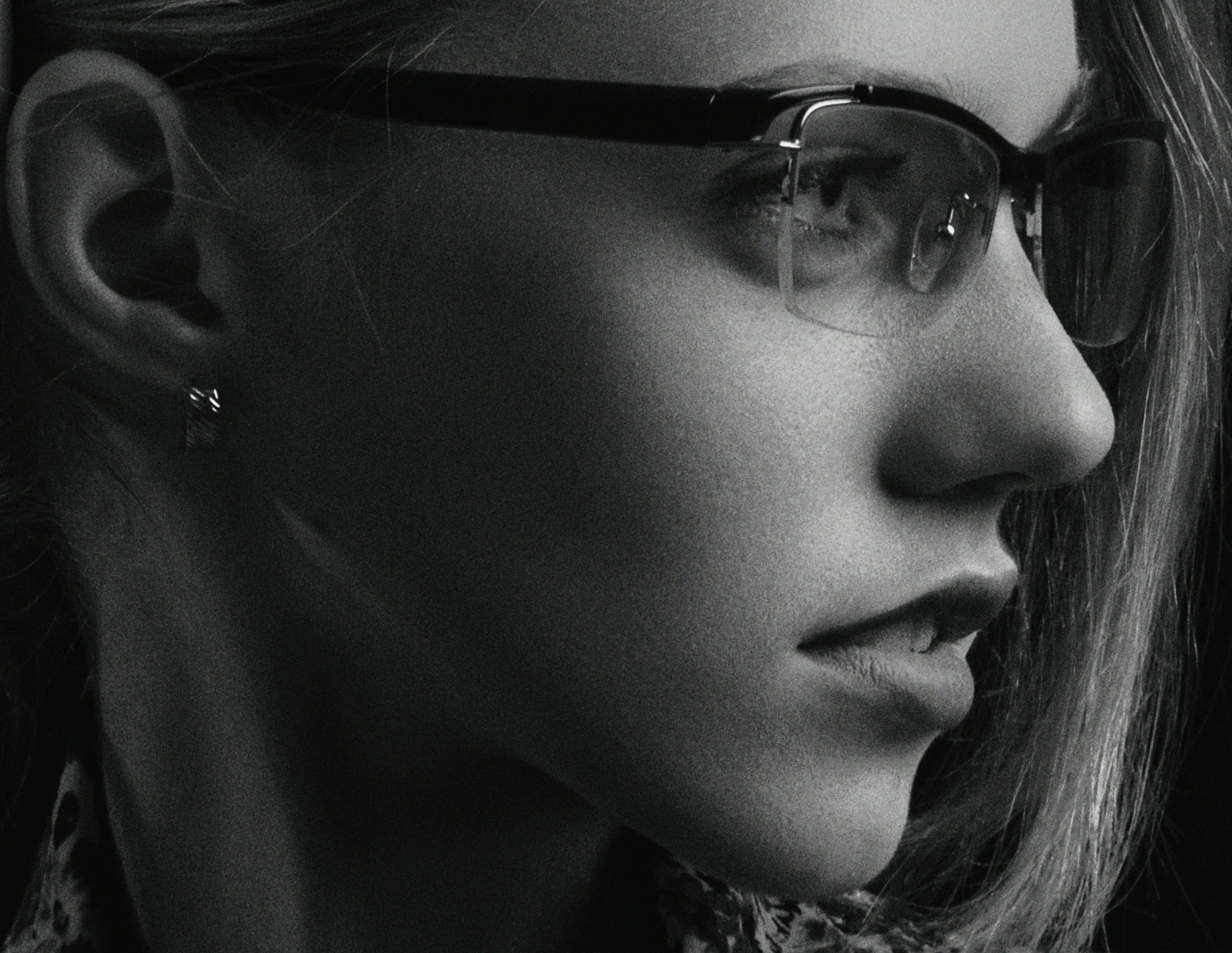 Close-up portrait of a woman wearing eyeglasses, captured in black and white.