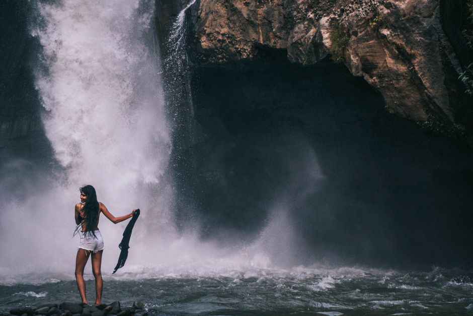 A woman poses in front of a majestic waterfall in Bali, creating a serene and adventurous scene.