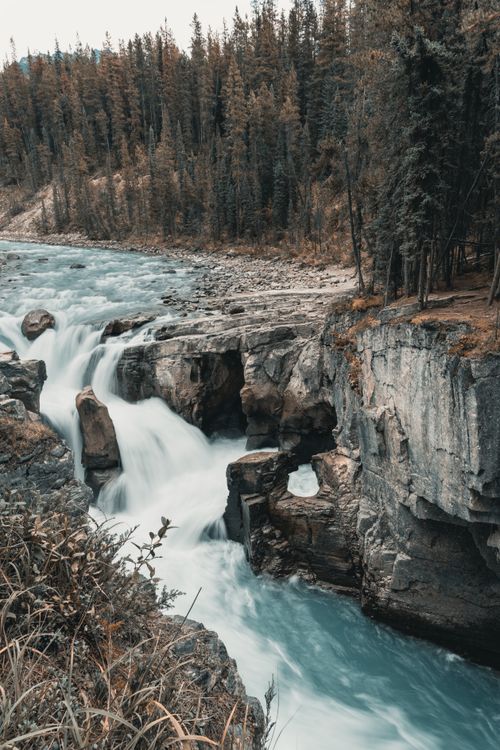 Free Captivating waterfall flowing through rugged rocks and lush forest in Jasper National Park, Canada. Stock Photo