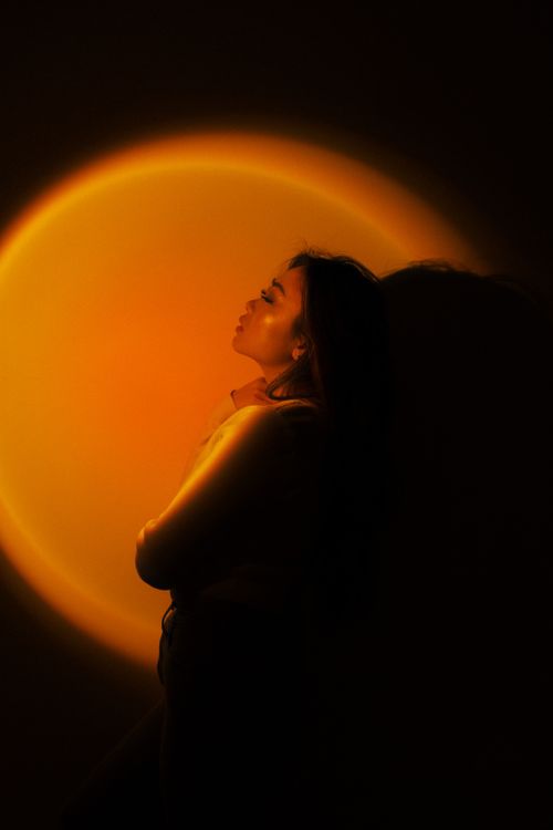 Free Captivating portrait of a woman with eyes closed against a glowing yellow background, creating a serene and dreamy atmosphere. Stock Photo