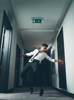 Stylish man striking a dance pose in a modern hallway with overhead lighting.