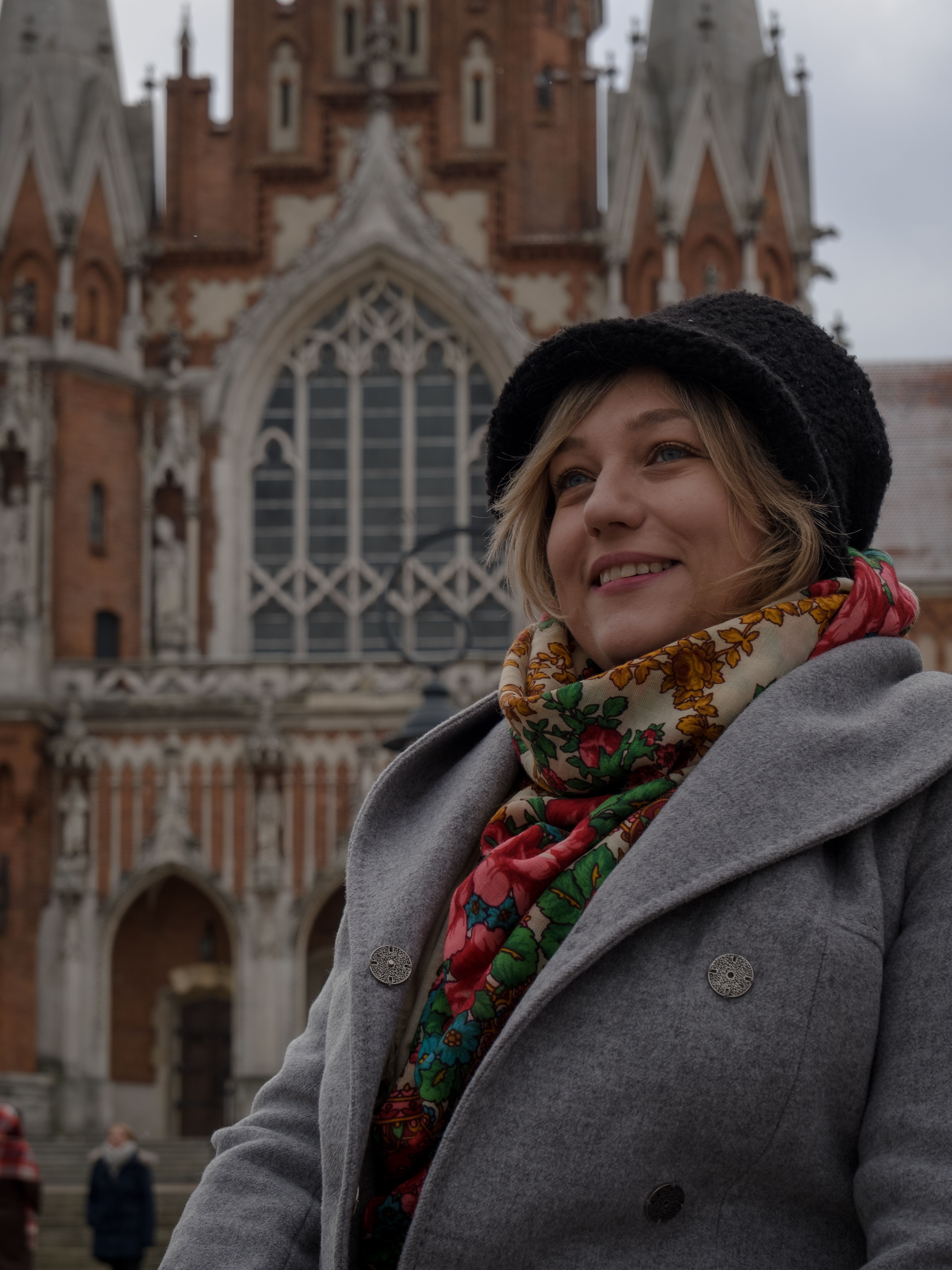 Smiling woman in a winter coat and scarf at St. Joseph's Church, Kraków, Poland.