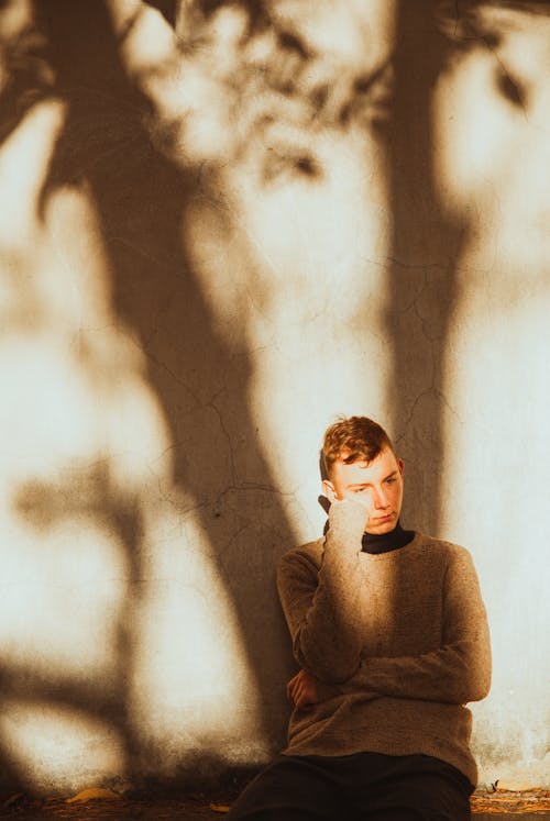Man Sitting near the Concrete Wall with His Hand Near His Face 