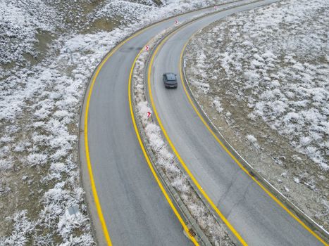 Aerial view of a snowy winding road in Ankara, Türkiye with a car navigating sharp curves.
