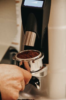 Close-up of a hand grinding coffee beans in a metal portafilter.