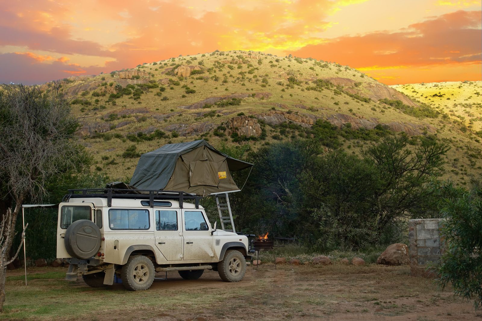 Stock image: a Land Rover with a rooftop tent beside a small fire in the Karoo at sunset