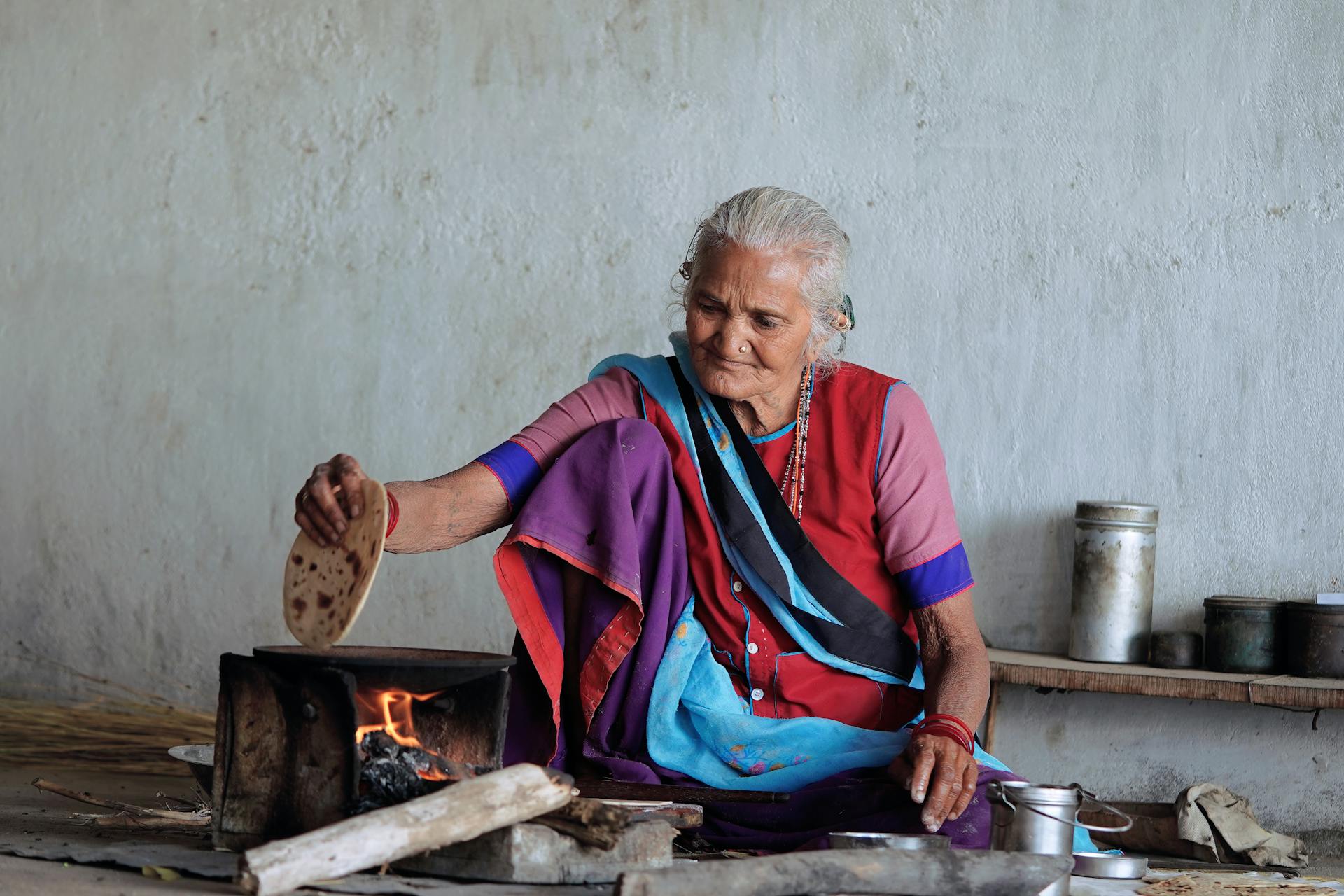 Senior woman in traditional attire making homemade Indian flatbread on an open fire.