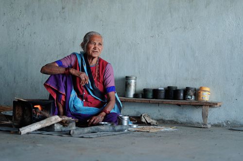 Free A senior woman sitting on the floor, cooking with traditional utensils, showcasing cultural heritage. Stock Photo