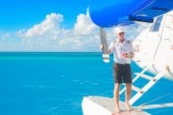 一名飞行员站在水上飞机上，飞机停在清澈的蓝色海洋中，天空中有云彩