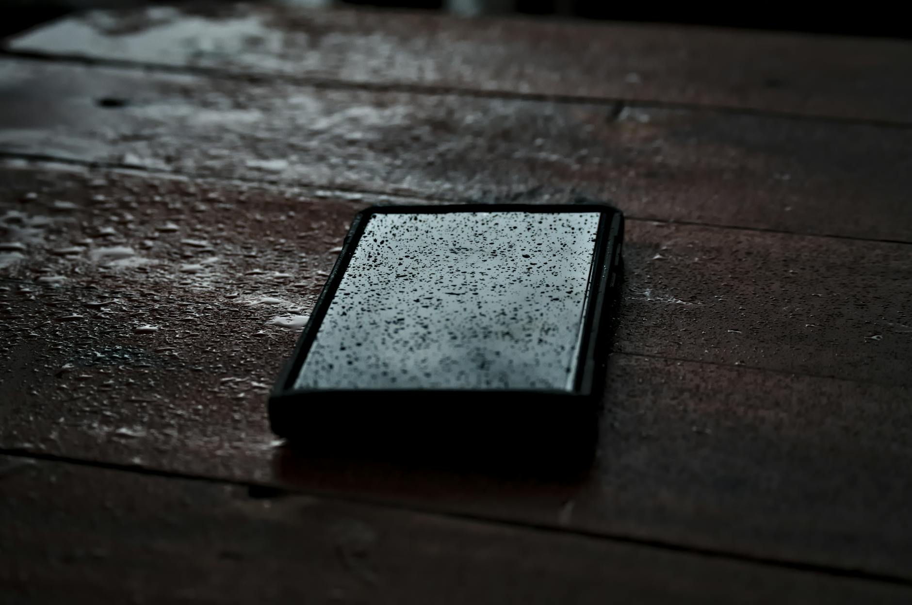 Close-up of a smartphone with droplets on a wet wooden surface, emphasizing waterproof technology