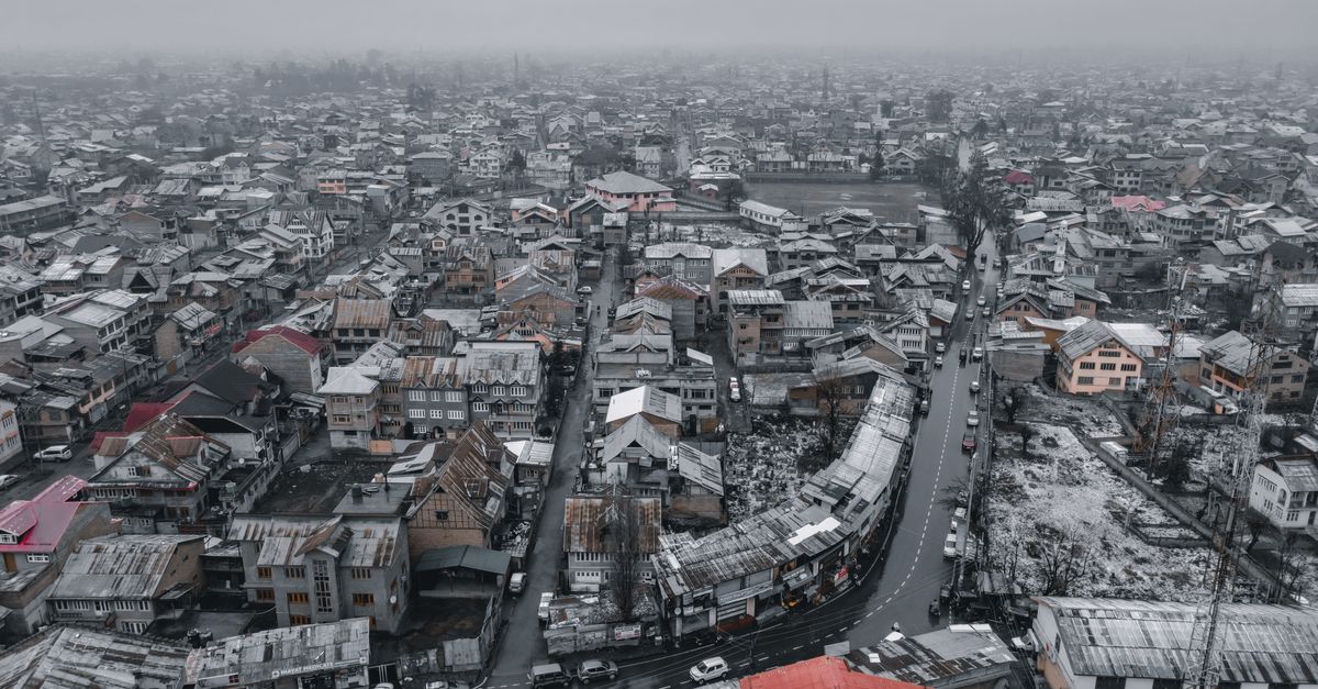 Aerial view of snowy Srinagar cityscape, showcasing rooftops and winding roads in winter.