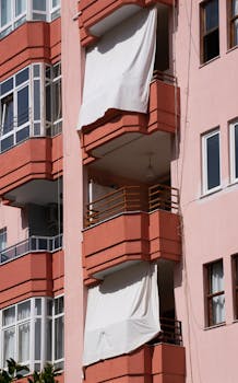 Close-up of residential building in Antalya featuring unique balconies with white drapes during a sunny day.