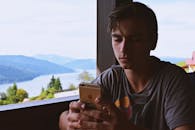 在罗马尼亚比卡兹，一名年轻男子在美丽的湖边用智能手机放松