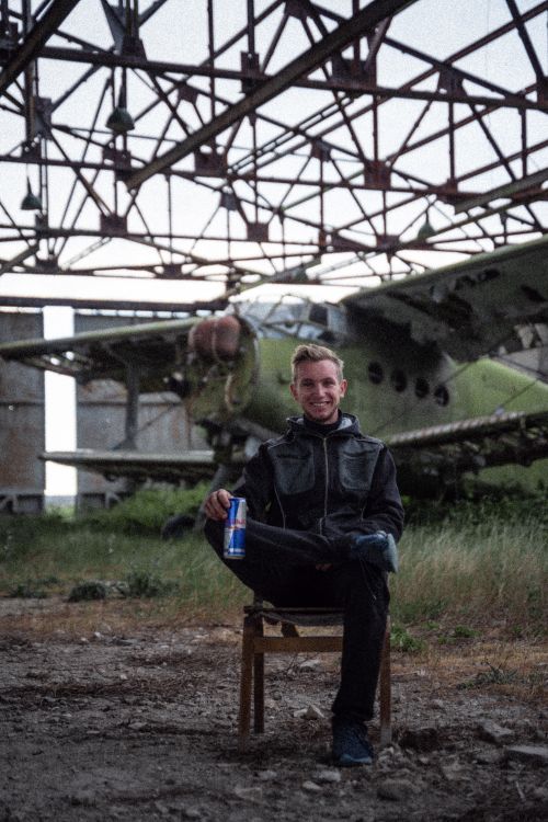 Free Man sitting with an energy drink in an abandoned industrial area featuring a biplane. Stock Photo