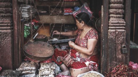 A woman vendor in traditional attire weighs spices at a vibrant street market, rich in cultural textures.