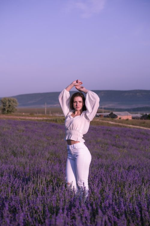 Free Woman with raised arms in a vibrant lavender field during sunset, showcasing peaceful fashion Stock Photo