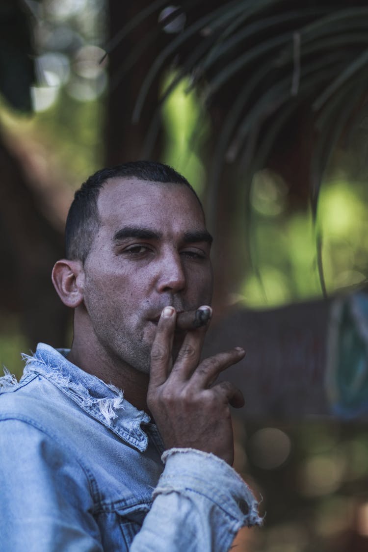 A Man In Denim Jacket Smoking Cigar While Looking At The Camera