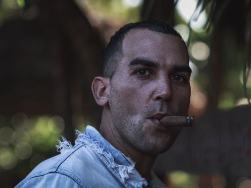 Free Portrait of a man smoking a cigar with a blurred natural background. Stock Photo