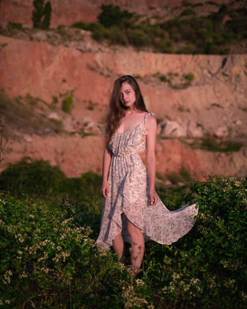 Free Woman stands gracefully in a floral dress against a rocky outdoor backdrop. Stock Photo