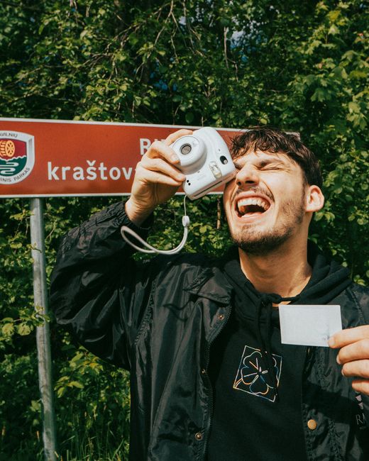 A cheerful young man photographing with an instant camera in a Vilnius park, Lithuania.