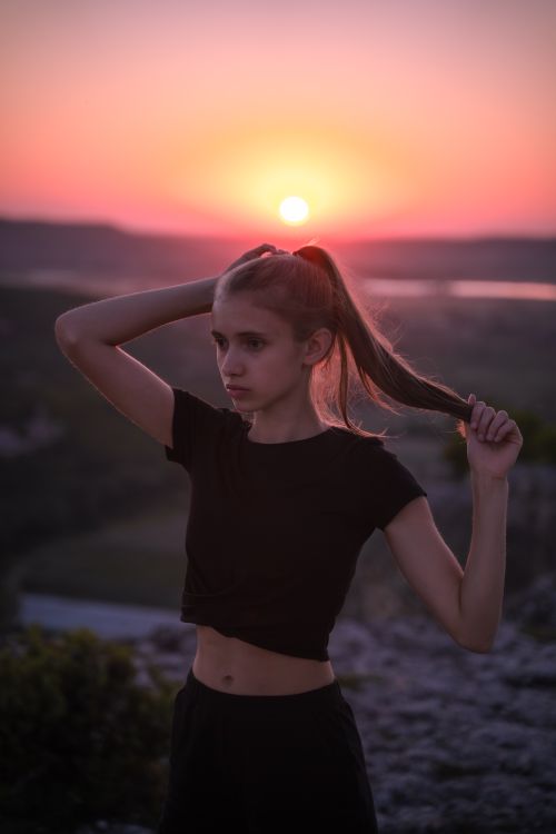 Free A young woman elegantly poses outdoors during a vivid sunset, blending with nature. Stock Photo