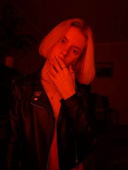 Stylized portrait of a woman with blond hair in a black jacket under red lighting. Artistic mood.
