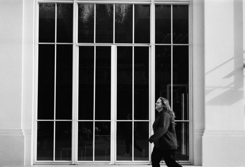 Free Candid shot of a woman walking past a large glass window in monochrome. Stock Photo