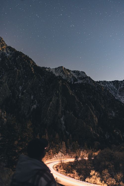 Free A person gazes at stars over a winding mountain road, showcasing nature's beauty. Stock Photo