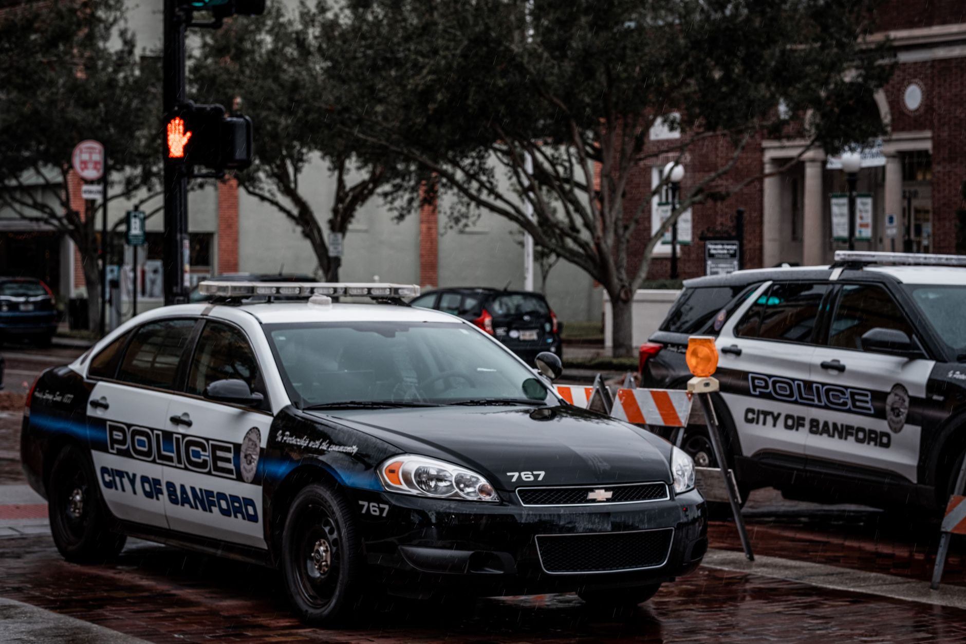City of Sanford police cars parked on wet urban streets with traffic signals and buildings.