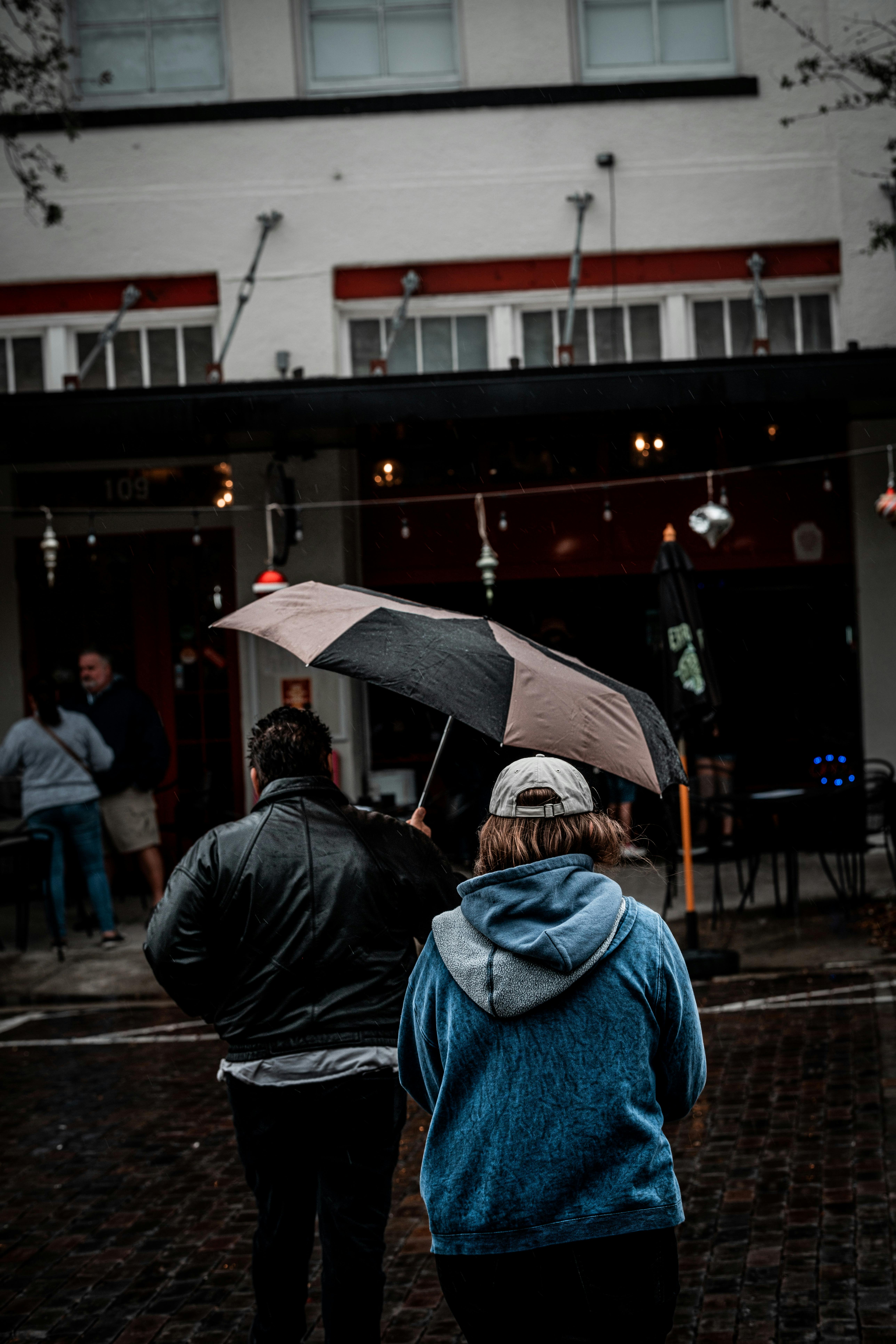 person in black jacket and blue denim jeans holding umbrella walking on sidewalk during nighttime