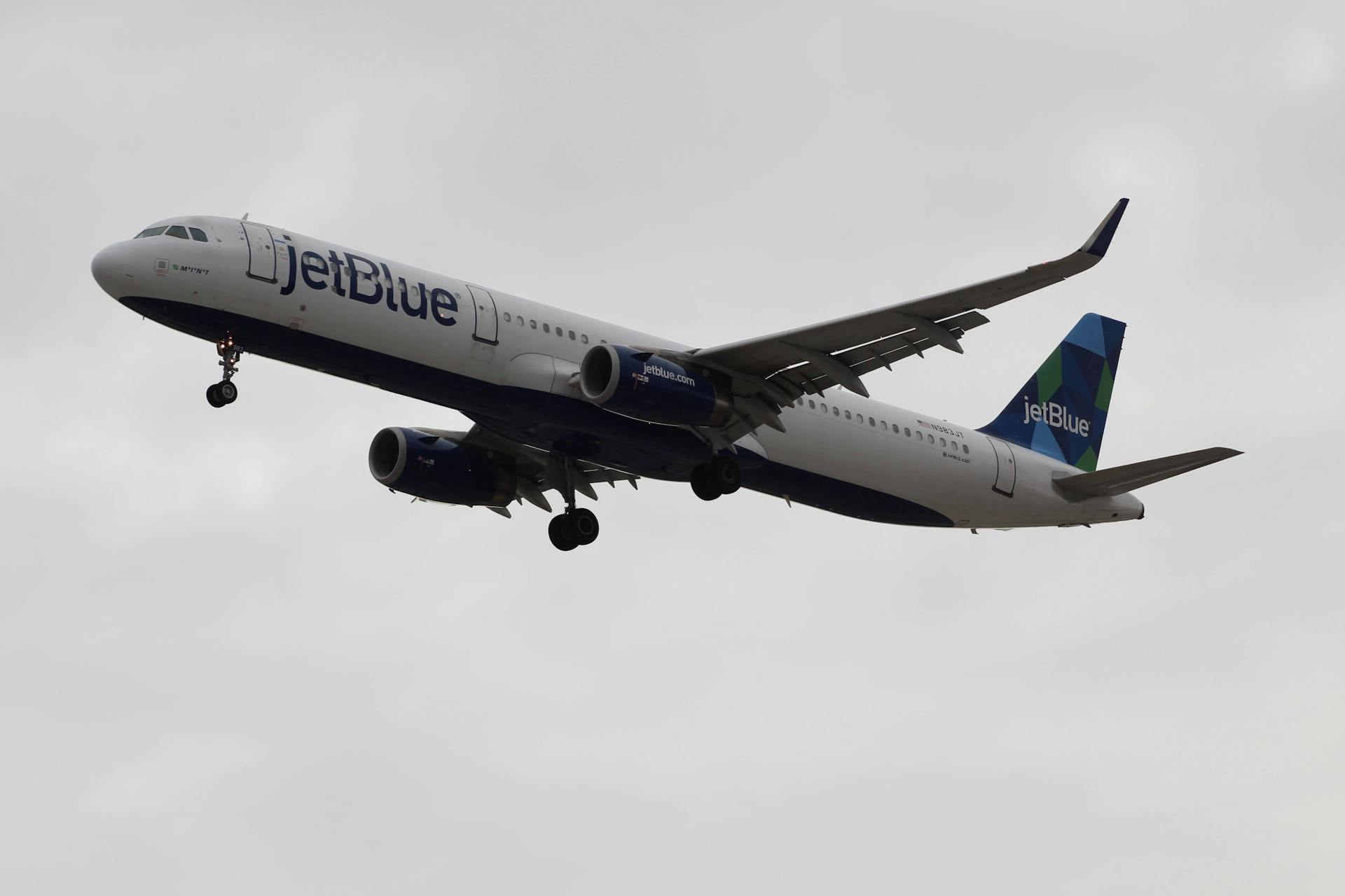 JetBlue airplane flying low against overcast sky, showcasing aviation dynamics.