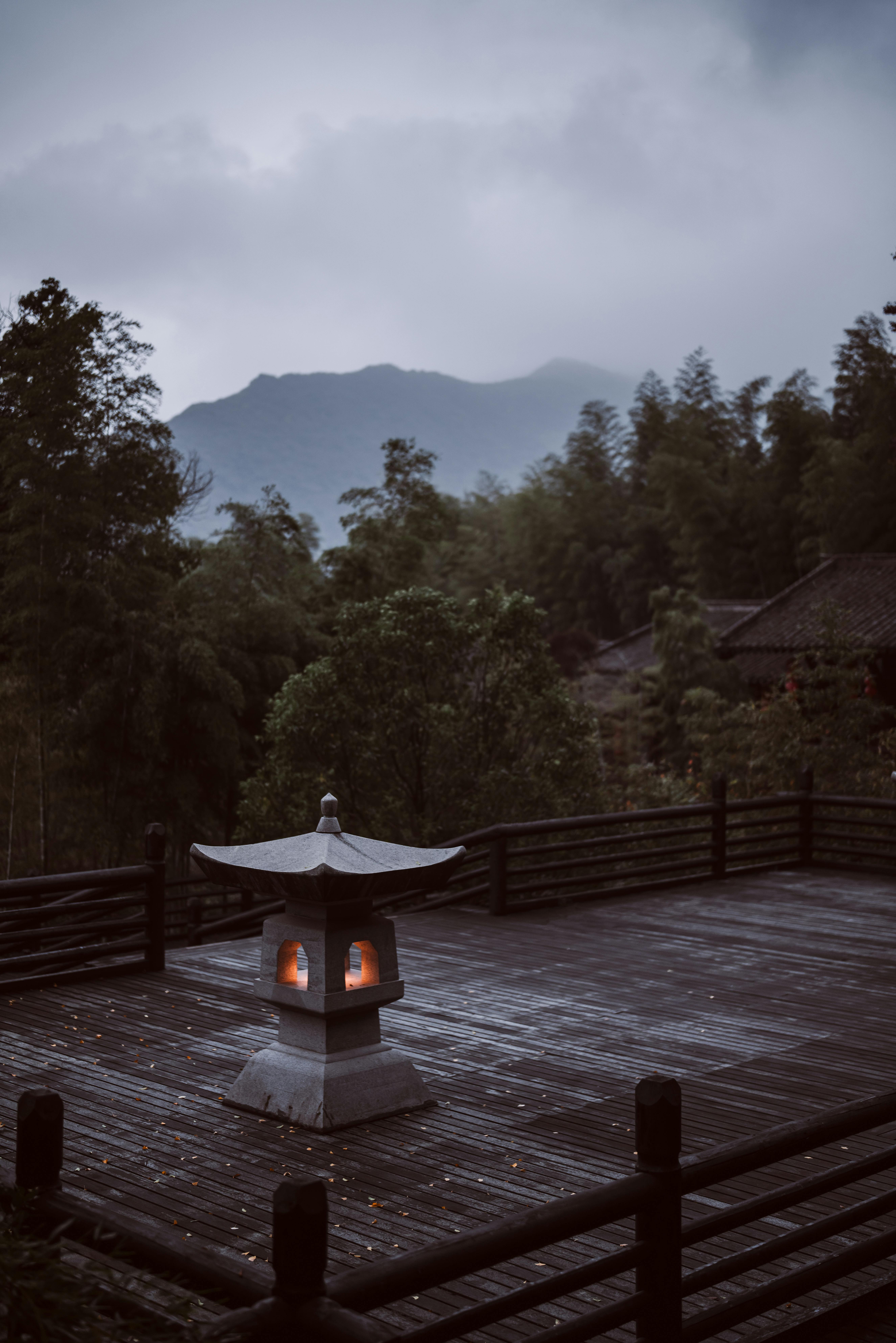 A tranquil outdoor scene with a lit lantern overlooking misty mountains and lush trees at dusk.