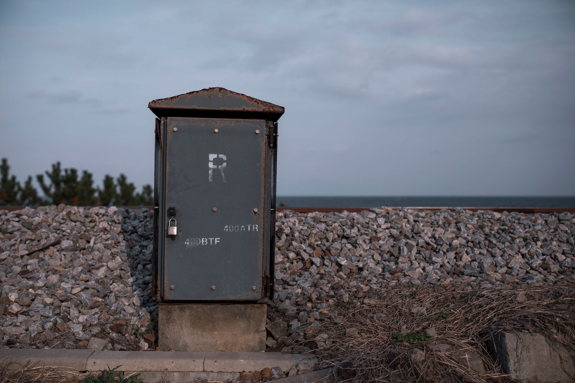 A rusty metal box secured by a padlock on a rocky shoreline in Donghae-si, South Korea.
