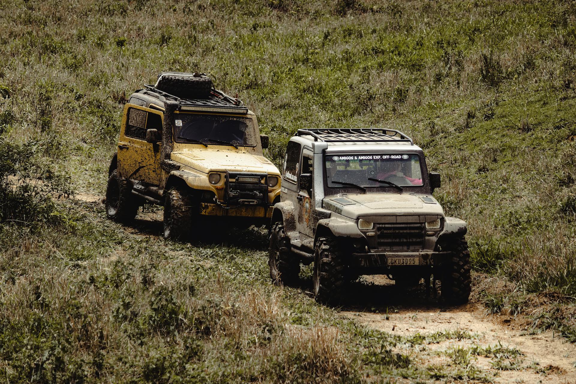 Two rugged 4x4 vehicles navigate a muddy path, showcasing off-road adventure spirit.