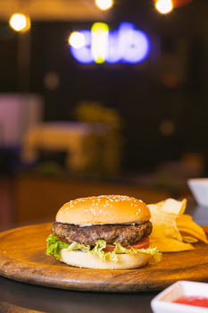 Mouth-watering beef burger with lettuce, tomato, and fries on a wooden plate in a cozy restaurant setting.